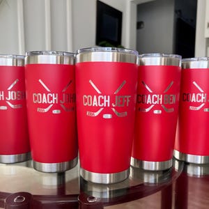 Op de afbeelding: Vijf rode ge&iuml;soleerde bekers met zilveren randen en bodems. Elke beker heeft een hockeystick- en puck-ontwerp, met de namen "COACH JOSH", "COACH JOHN", "COACH JEFF", "COACH BEN" en "COACH JUSTIN" gegraveerd.
