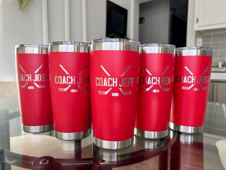 Op de afbeelding: Vijf rode ge&iuml;soleerde bekers met zilveren randen en bodems. Elke beker heeft een hockeystick- en puck-ontwerp, met de namen "COACH JOSH", "COACH JOHN", "COACH JEFF", "COACH BEN" en "COACH JUSTIN" gegraveerd.