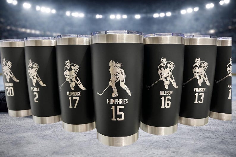 Op de afbeelding: Zwarte ge&iuml;soleerde bekers met zilveren accenten, elk met een hockey speler afbeelding en een naam en nummer. Deze bekers zijn ideaal voor sportfans en voor warme of koude dranken.