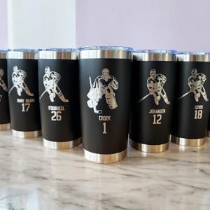 Op de afbeelding: Zwarte ge&iuml;soleerde bekers met zilveren deksels en bodems. Elke beker heeft een zilveren hockey speler afbeelding en een naam of nummer. De bekers zijn gepersonaliseerd met namen en nummers.
