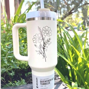 May include: Cream-colored Stanley Quencher H2.0 tumbler with a white handle and lid, and a clear straw. The tumbler features a floral design with the date 03.10.2025. The tumbler is 40 oz / 1.18 L and is designed for all-day hydration.