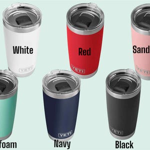 Op de afbeelding: Zes ge&iuml;soleerde bekers in verschillende kleuren: wit, rood, zandsteen, zeegroen, marineblauw en zwart. Elke beker heeft een zilveren deksel en de merknaam "YETI" op de voorkant. De bekers zijn ontworpen om dranken koud of warm te houden.
