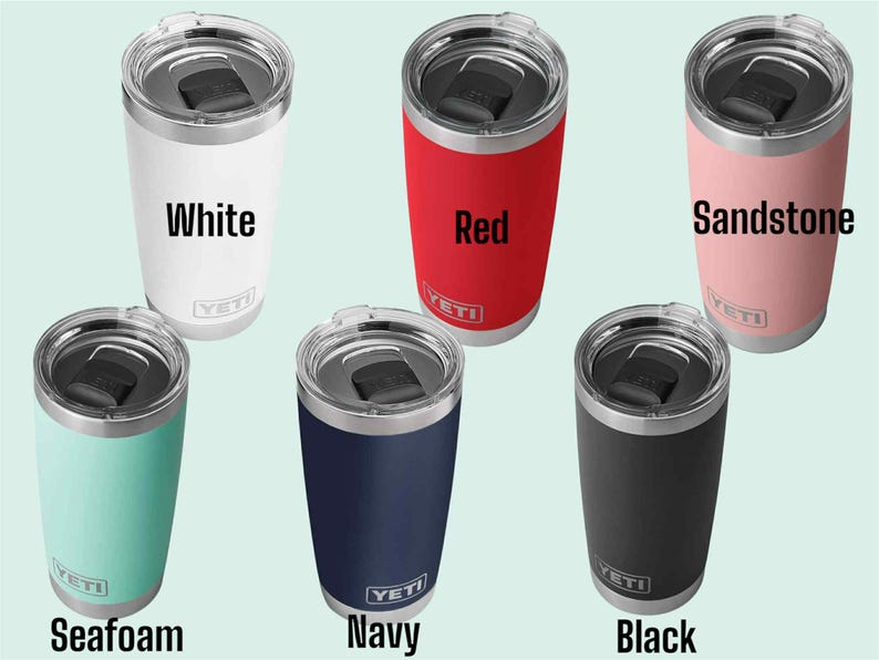 Op de afbeelding: Zes ge&iuml;soleerde bekers in verschillende kleuren: wit, rood, zandsteen, zeegroen, marineblauw en zwart. Elke beker heeft een zilveren deksel en de merknaam "YETI" op de voorkant. De bekers zijn ontworpen om dranken koud of warm te houden.