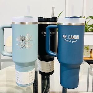 May include: Three insulated tumblers with handles and straws. One is light blue with "Ms. Jim" and floral design, another is black, and the third is blue with "MR. CANON Thank you!" text. All have white lids.