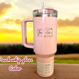 May include: A peach-colored tumbler with a handle, a clear lid, and a straw. The text "BEST Teacher EVER" is printed on the front. The words "Peach whip gloss Color" are written in a cursive font at the bottom.