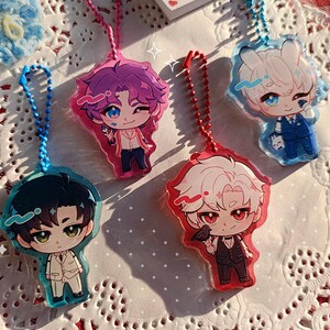 K&ouml;nnte beinhalten: Vier Anime-Stil Acryl-Anh&auml;nger mit Schl&uuml;sselanh&auml;ngern. Jeder Anh&auml;nger zeigt einen Chibi-Charakter mit unterschiedlichen Haaren und Kleidung. Die Anh&auml;nger sind in Blau, Rosa und Rot gehalten, mit detaillierten Gesichtsz&uuml;gen und Outfits. Sie werden auf einer wei&szlig;en Spitzentischdecke pr&auml;sentiert.