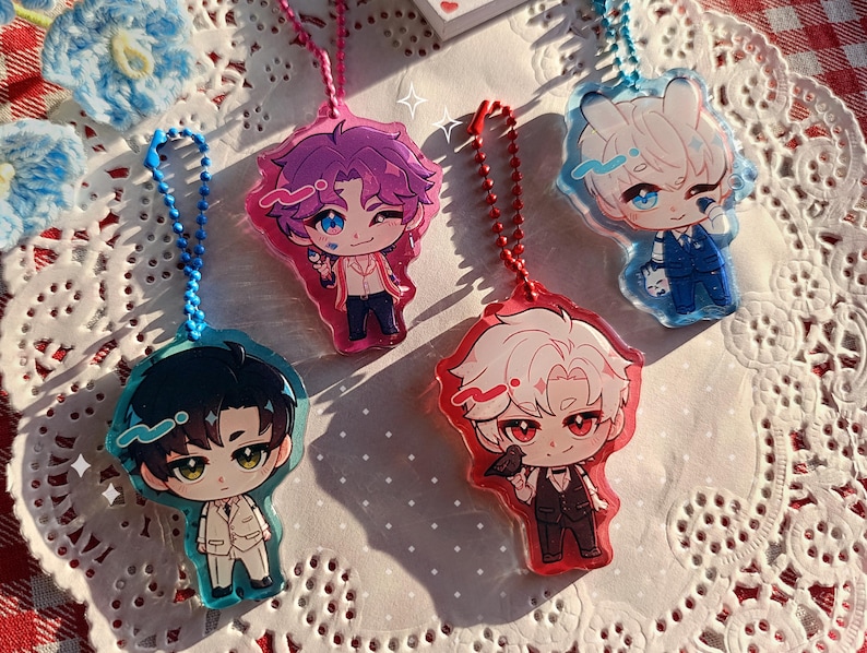 K&ouml;nnte beinhalten: Vier Anime-Stil Acryl-Anh&auml;nger mit Schl&uuml;sselanh&auml;ngern. Jeder Anh&auml;nger zeigt einen Chibi-Charakter mit unterschiedlichen Haaren und Kleidung. Die Anh&auml;nger sind in Blau, Rosa und Rot gehalten, mit detaillierten Gesichtsz&uuml;gen und Outfits. Sie werden auf einer wei&szlig;en Spitzentischdecke pr&auml;sentiert.