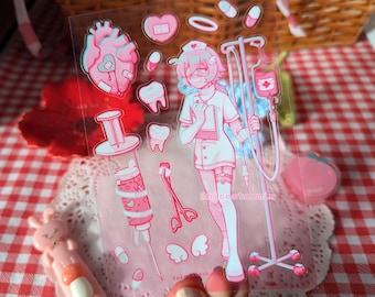 Puede incluir: Una hoja de pegatinas transparente con ilustraciones médicas en tonos rosas que incluyen un personaje de enfermería, un soporte para gotero, una jeringa grande, un corazón, dientes, pastillas y alas. El texto "nisestarmin" aparece impreso.