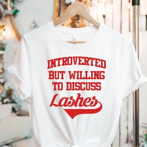 May include: White t-shirt with red text that reads "Introverted but willing to discuss lashes".