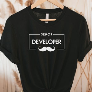 May include: Black t-shirt with white text that reads "Señor Developer" and a white moustache graphic.