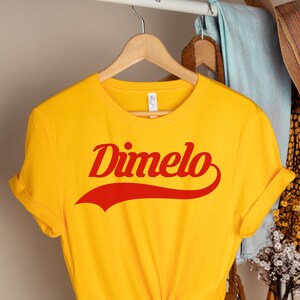 May include: Yellow t-shirt with a red "Dimelo" graphic in a retro font style.