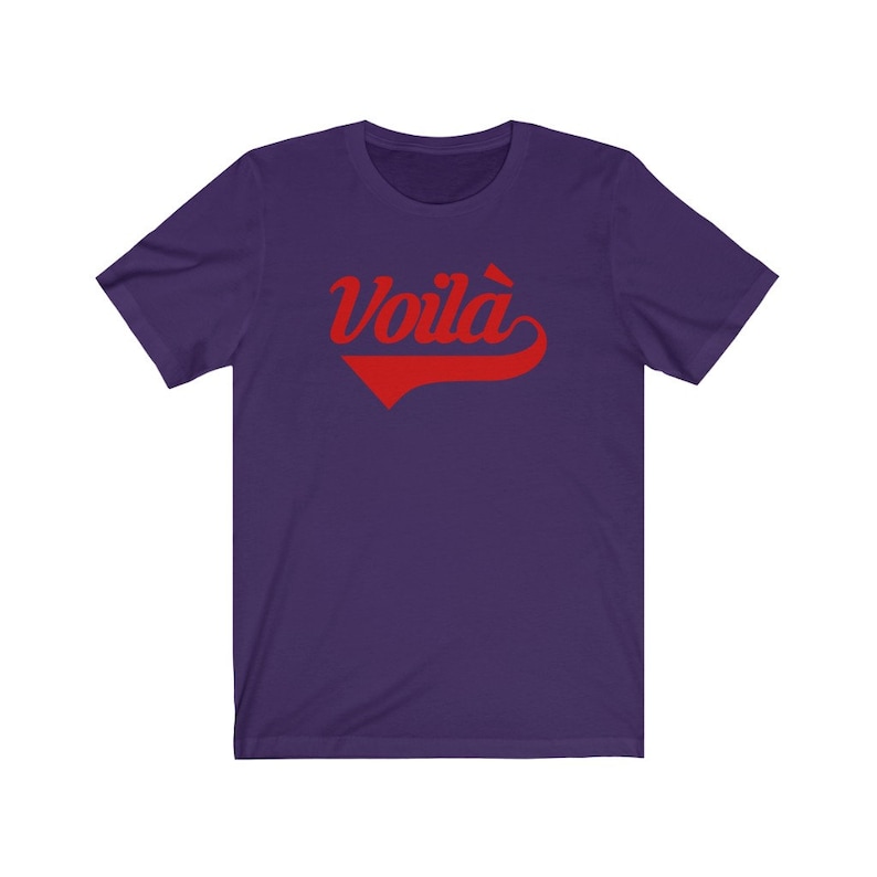 Puede incluir: Camiseta de manga corta de color morado con un gr&aacute;fico rojo "Voil&agrave;" en una fuente de b&eacute;isbol vintage.