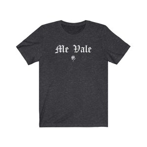 May include: A dark heather grey t-shirt with the text "Me Vale" in white gothic lettering and a small white rose graphic.