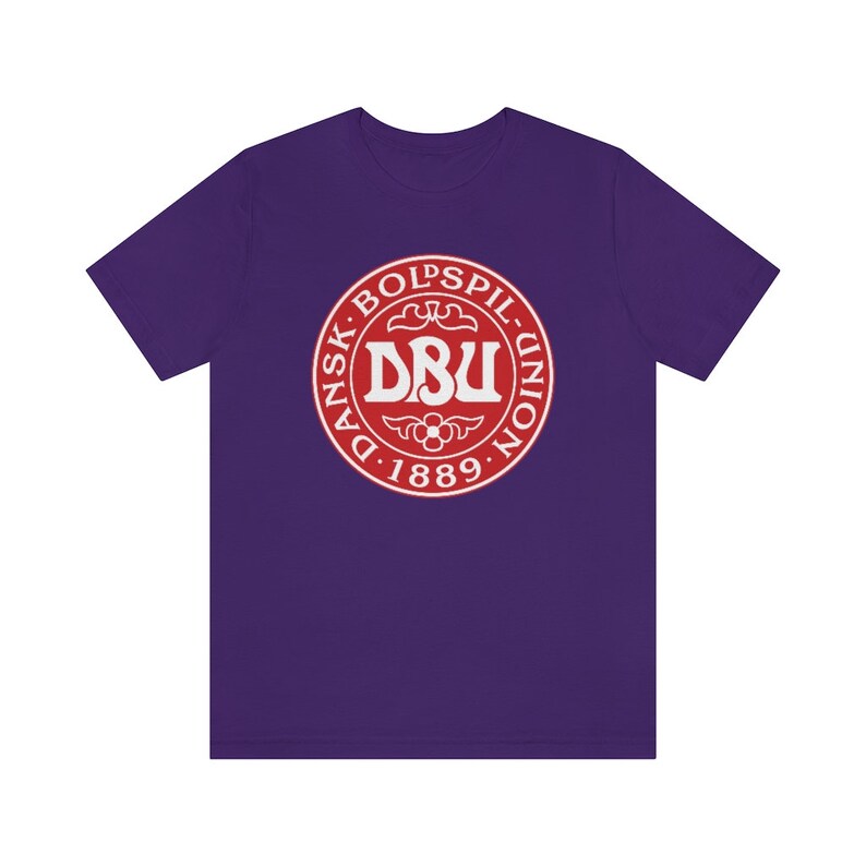 Puede incluir: Camiseta morada con un logotipo rojo y blanco que dice "Dansk Boldspil-Union D. 1889."
