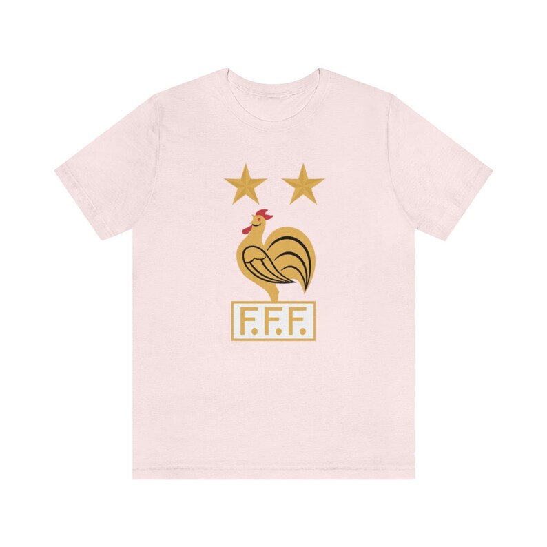 May include: A pink t-shirt with a gold rooster and two stars above it. The rooster is standing on a white rectangle with the letters "F.F.F." printed on it.