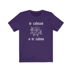 May include: Purple t-shirt with white text that reads "te calmas o te calmo" and a white rose graphic.