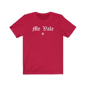 May include: Red short-sleeved t-shirt with white text that reads "Me Vale" in a gothic font. A small white rose is below the text.