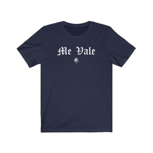 May include: A navy blue t-shirt with the text "Me Vale" in white, old English lettering. A small white rose is below the text.