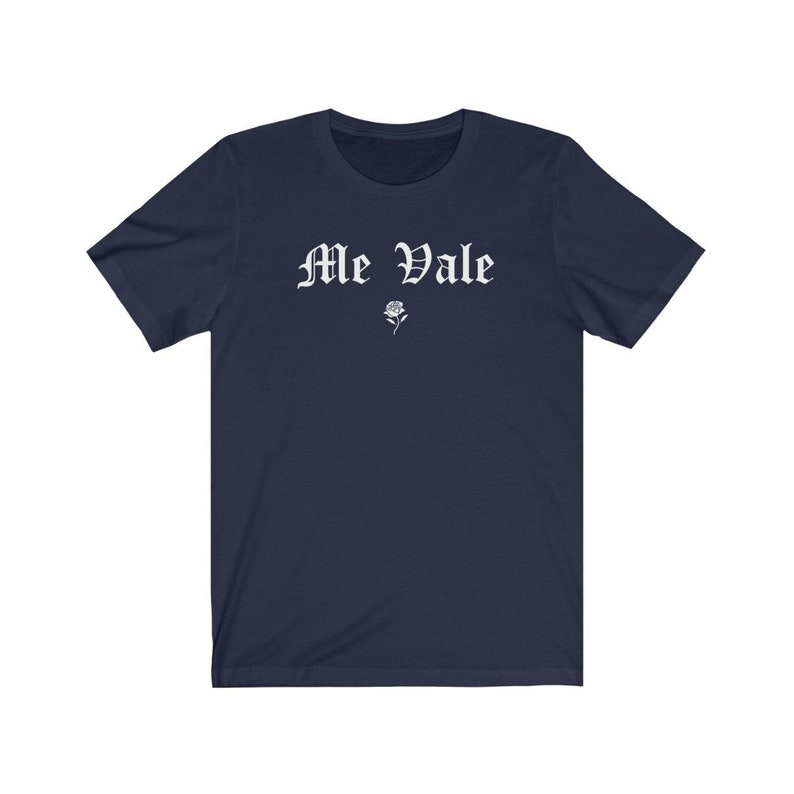 May include: A navy blue t-shirt with the text "Me Vale" in white, old English lettering. A small white rose is below the text.