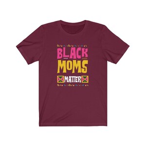 May include: Burgundy t-shirt with the text "Black Moms Matter" in pink, yellow, and black lettering. The text is surrounded by a colorful geometric pattern.