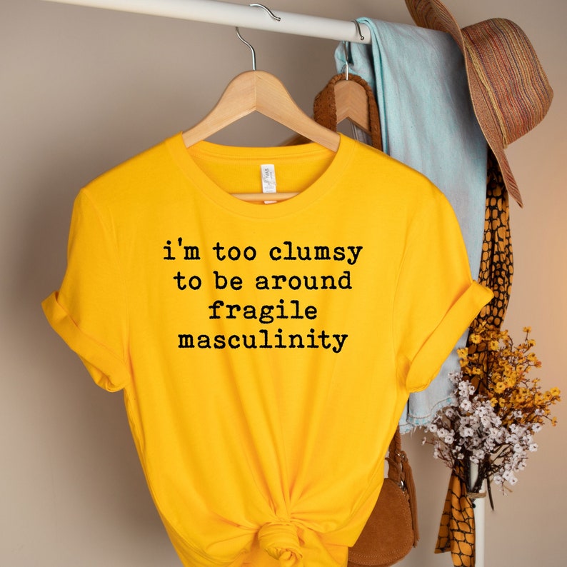 Puede incluir: Camiseta amarilla con el texto "i'm too clumsy to be around fragile masculinity" impreso en negro.