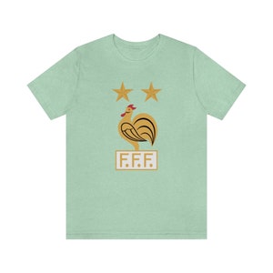 May include: A light green t-shirt with a gold rooster and two gold stars above it. The rooster is standing on a white rectangle with the text "F.F.F." in gold letters.