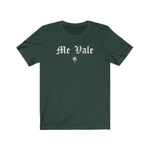 May include: A dark green t-shirt with the text "Me Vale" in white gothic lettering and a small white rose graphic.