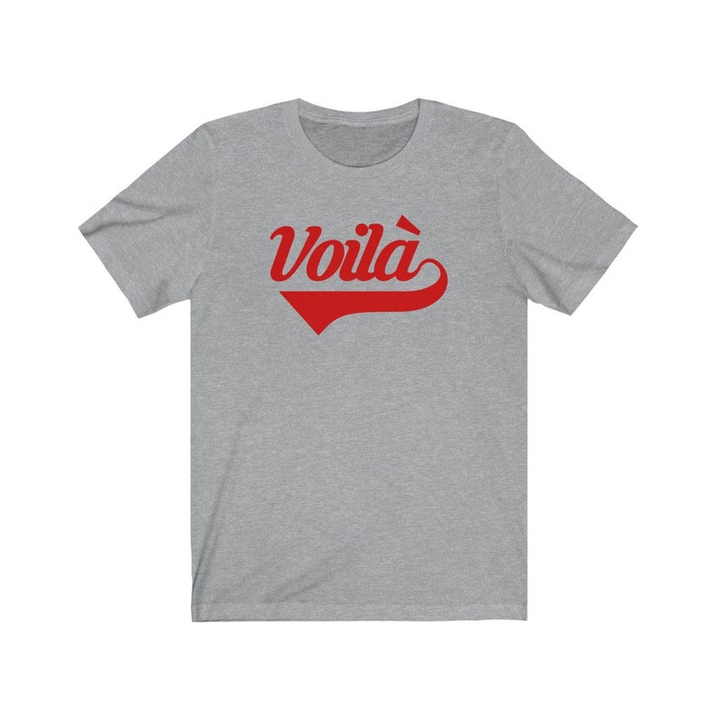 Puede incluir: Una camiseta gris jaspeada con un gr&aacute;fico rojo "Voila!" en una fuente de b&eacute;isbol vintage.