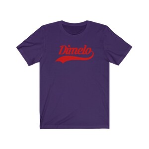 May include: Purple short-sleeved t-shirt with the word "Dimelo" in red, stylized text with a curved red line underneath.