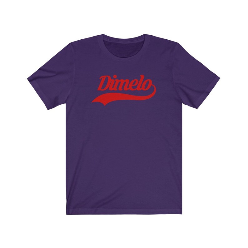 May include: Purple short-sleeved t-shirt with the word "Dimelo" in red, stylized text with a curved red line underneath.