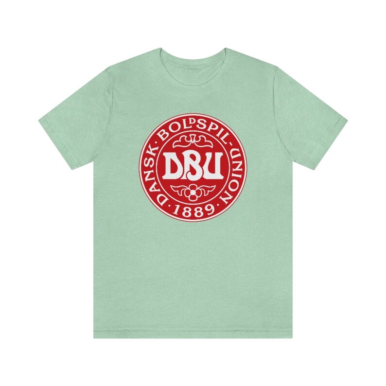 Puede incluir: Una camiseta verde claro con un logotipo circular rojo. El logotipo dice "Dansk Boldspil-Union DBU 1889" en texto blanco.