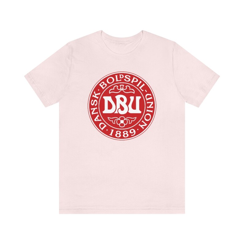 Puede incluir: Una camiseta rosa con un logotipo circular rojo. El logotipo dice "Dansk Boldspil-Union DBU 1889" en letras blancas.
