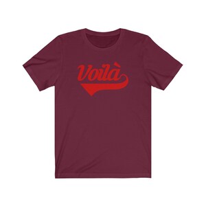Puede incluir: Una camiseta color burdeos con un gr&aacute;fico rojo "Voil&agrave;" en una fuente de b&eacute;isbol vintage.