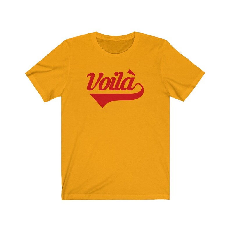 Puede incluir: Una camiseta amarilla de manga corta con un gr&aacute;fico rojo "Voila!" en una fuente retro.