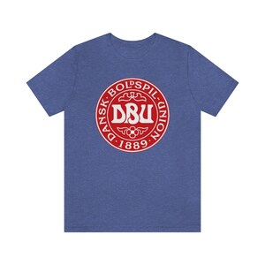 Puede incluir: Una camiseta azul con un logotipo circular rojo. El logotipo dice "Dansk Boldspil-Union DBU 1889".