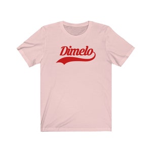 May include: A pink t-shirt with a red "Dimelo" graphic in a vintage baseball font.