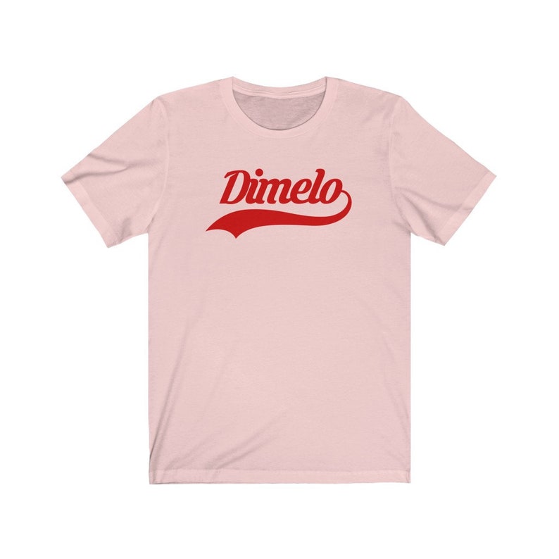 May include: A pink t-shirt with a red "Dimelo" graphic in a vintage baseball font.