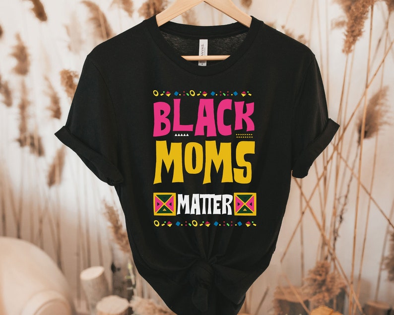 May include: Black t-shirt with the text "Black Moms Matter" in pink, yellow, and green lettering. The text is surrounded by a colorful geometric pattern.