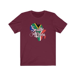 May include: A maroon t-shirt with a graphic of the outline of South Africa with the South African flag colors and the text "South Africa" in white cursive.