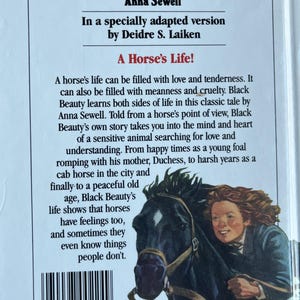 Op de afbeelding: Boekomslag van "Black Beauty" van Anna Sewell, bewerkt door Deidre S. Laiken. Het toont een zwart paard met een ruiter. De titel is blauw en de tekst beschrijft het leven van een paard, met een barcode onderaan.