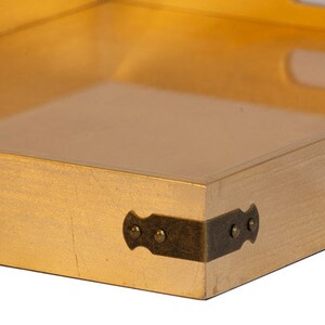 May include: A gold-colored wooden tray with a clear glass insert and brass corner accents. The tray has a rectangular shape and is perfect for serving snacks or drinks.
