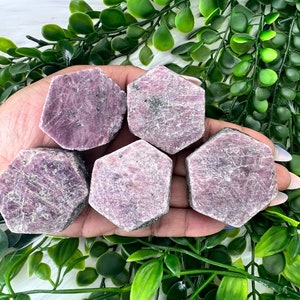 May include: Five pink ruby crystal points in a hexagonal shape. The crystals are raw and have a natural, rough texture.