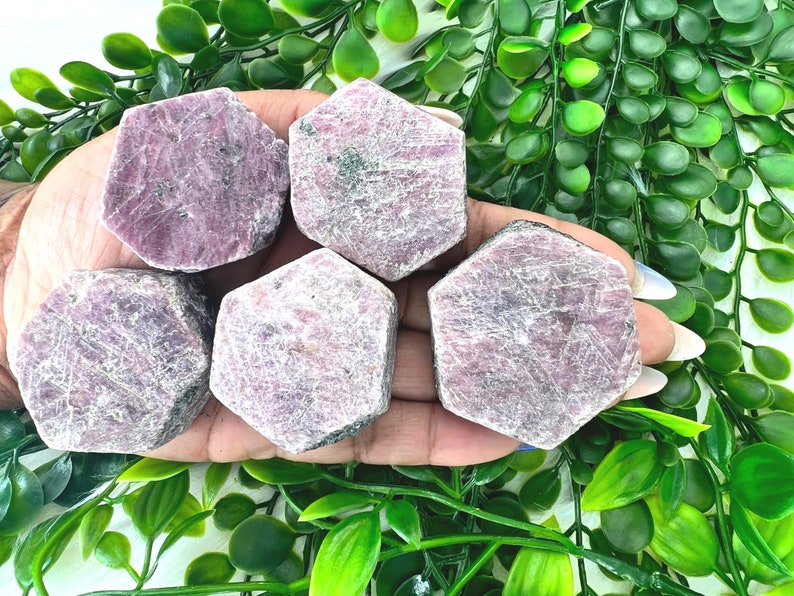 May include: Five pink ruby crystals in a hexagonal shape, with a rough, natural texture. The crystals are arranged in a hand, with the tips of the crystals pointing towards the viewer.