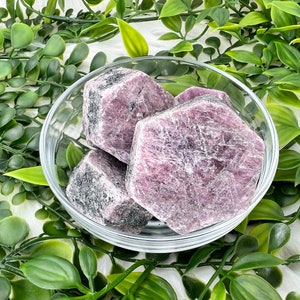 May include: Four rough-cut pink and purple gemstone crystals in a clear glass bowl. The crystals are in a variety of shapes and sizes.
