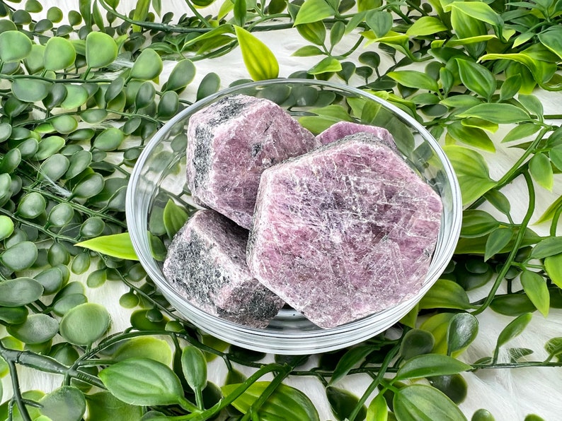 May include: Four rough-cut pink and purple gemstone crystals in a clear glass bowl. The crystals are in a variety of shapes and sizes.