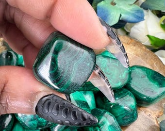 May include: A collection of tumbled malachite stones, each with a unique green and black pattern. The stones are smooth and polished, with a natural, earthy look.