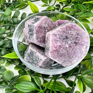 May include: Four rough-cut purple and grey ruby crystals in a clear glass bowl. The crystals are arranged in a cluster, with the largest crystal in the centre.