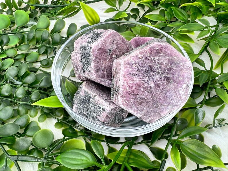 May include: Four rough-cut purple and grey ruby crystals in a clear glass bowl. The crystals are arranged in a cluster, with the largest crystal in the centre.