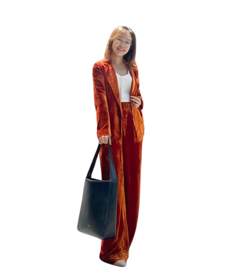 May include: A burnt orange velvet pantsuit with a matching blazer and wide-leg trousers. The outfit is paired with a white top and a black tote bag. The ensemble is a stylish, monochromatic look.