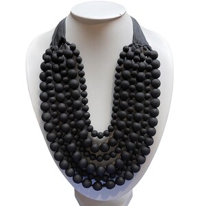 May include: A black beaded necklace displayed on a white mannequin bust. The necklace features multiple strands of matte black beads of varying sizes, creating a layered effect. The necklace is secured with a dark gray ribbon.